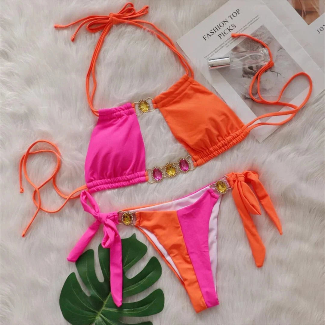 Bikini strass rose fuchsia et orange posé à plat sur une fourrure blanche, feuille verte à côté et liens longs à nouer