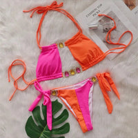 Bikini strass rose fuchsia et orange posé à plat sur une fourrure blanche, feuille verte à côté et liens longs à nouer