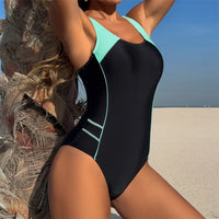 Maillot de bain une pièce dos nu échancré noir et bleu turquoise vu de côté sur le sable, liserés bleu clair sur la hanche