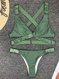 Bikini sans armatures croisé dans le dos vert kaki posé à plat sur un tapis gris, bretelles croisées et sangle centrale