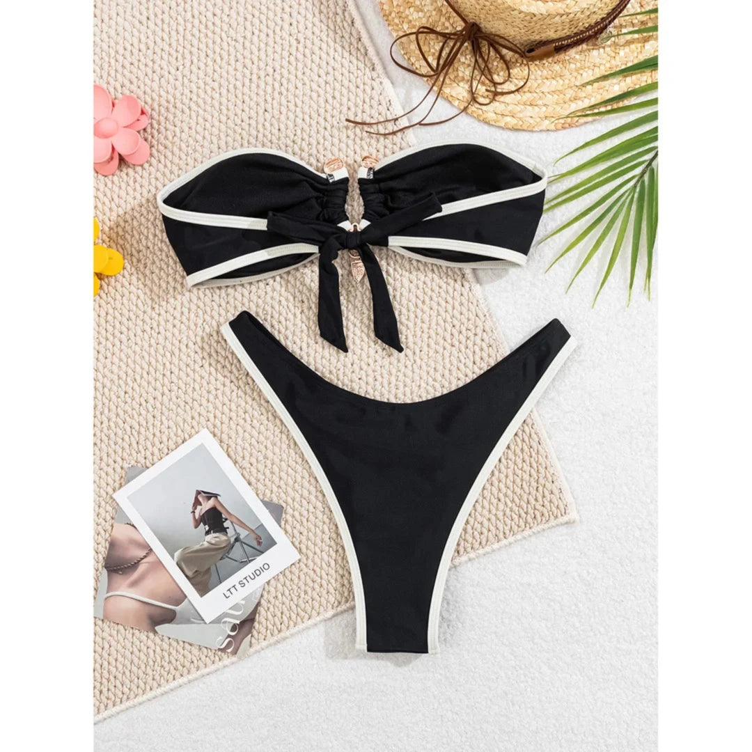 Bikini bandeau brésilien à anneau métallique noir à liseré crème posé à plat sur un tapis beige, bandeau noué devant