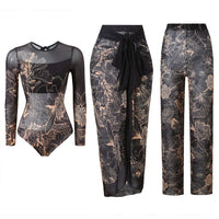 Maillot trois pièces manches longues noir à fleurs dessinées beiges, body, paréo et pantalon en mesh posés à plat