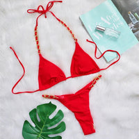 Bikini string tour de cou à anneau métallique froncé rouge posé à plat sur fourrure blanche, magazine et feuille verte