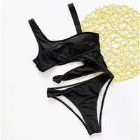 Maillot de bain une pièce échancré noir posé à plat à côté d'un tissu jaune, découpe horizontale et bretelle unique