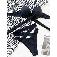 Bikini à armatures taille haute croisé effet bandage noir posé à plat sur un tissu zèbre et un magazine