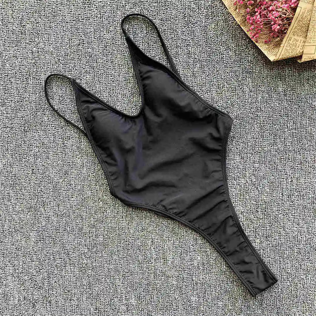 Maillot de bain une pièce noir à plat sur un tapis gris, bretelles fines et coupe string haute