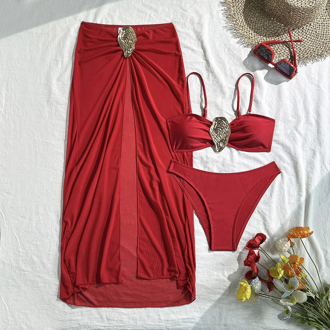 Maillot trois pièces rouge posé à plat avec jupe longue et anneau doré, bas taille basse, fleurs et lunettes en décor