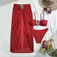 Maillot trois pièces rouge posé à plat avec jupe longue et anneau doré, bas taille basse, fleurs et lunettes en décor