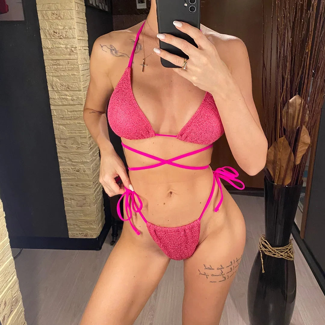 Bikini croisé rose vif pailleté porté de face devant un mur en pierre, lanières croisées autour du torse et bas noué