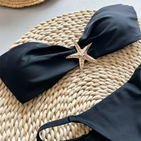 Gros plan sur l'étoile métallique dorée du bikini bandeau string échancré noir, tissu lisse du haut en arrière-plan