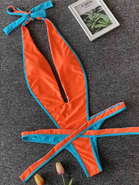 Maillot une pièce orange à bordures bleu turquoise posé à plat sur une moquette grise, livre à côté