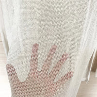 Gros plan sur le mesh blanc cassé d'une tunique de plage, la texture ajourée laisse apparaître une main dessous