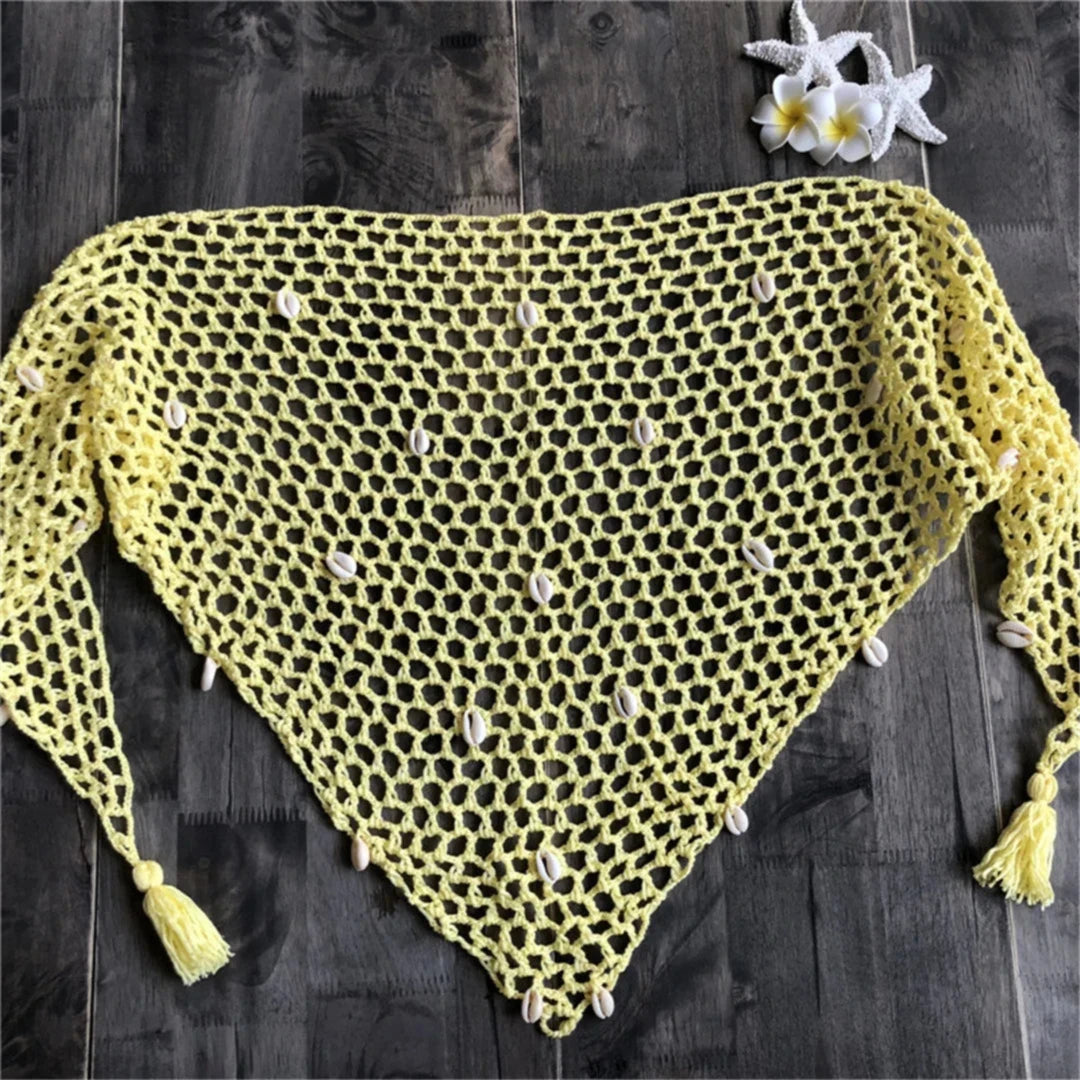 Gros plan sur un angle du paréo jaune en crochet, mailles ajourées et pompon en bas sur bois sombre