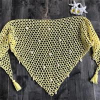 Gros plan sur un angle du paréo jaune en crochet, mailles ajourées et pompon en bas sur bois sombre