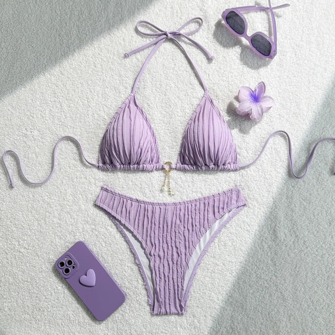 Bikini brésilien tour de cou effet froissé violet à plat avec lunettes, fleur violette et téléphone à côté
