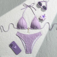 Bikini brésilien tour de cou effet froissé violet à plat avec lunettes, fleur violette et téléphone à côté