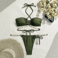 Bikini vert kaki à coquillages posé à plat avec des fleurs blanches et une sandale, bas à liens noués
