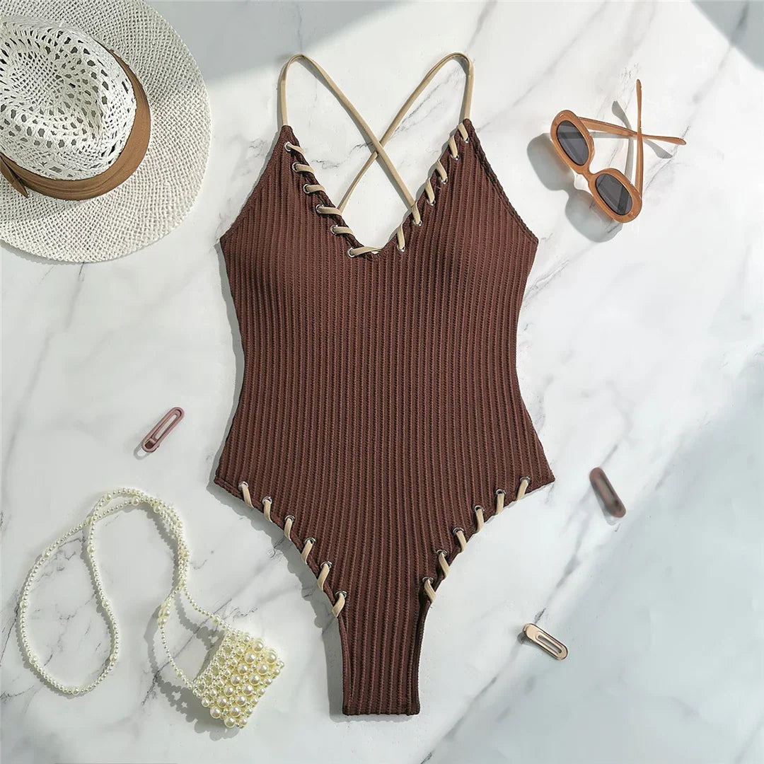 Maillot de bain une pièce côtelé marron foncé posé à plat sur marbre, lacets beiges le long des bordures