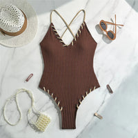 Maillot de bain une pièce côtelé marron foncé posé à plat sur marbre, lacets beiges le long des bordures