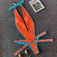 Maillot une pièce orange à liseré bleu posé à plat sur une moquette grise, lanières croisées et petite plante