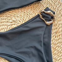 Gros plan sur l'anneau métal doré du maillot de bain une pièce asymétrique noir, bord de la découpe latérale