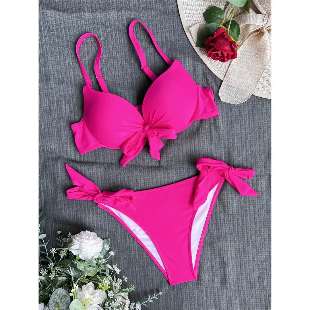 Bikini push-up noué avec armatures et rembourrage rose fuchsia posé à plat sur tissu gris, nœuds central et latéraux