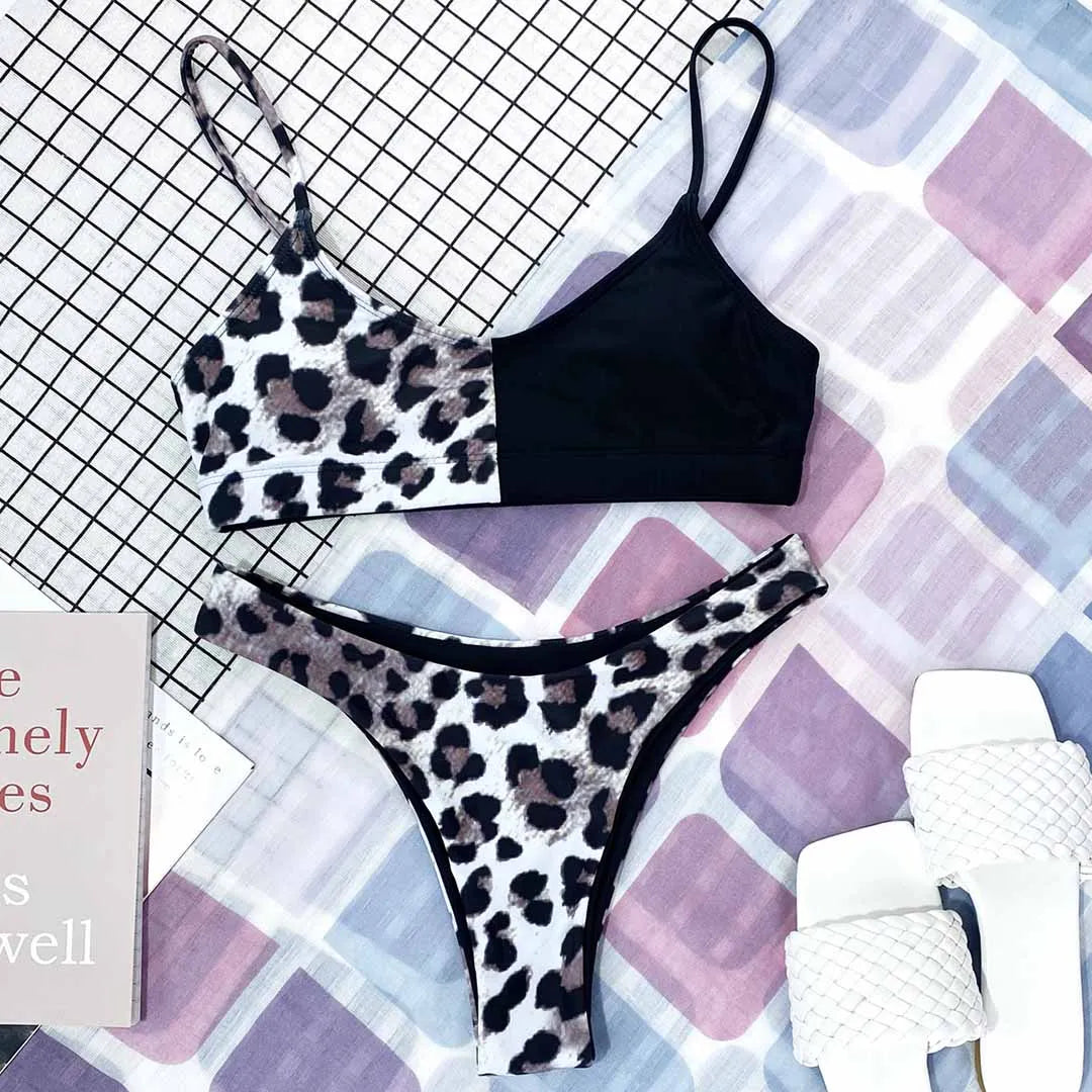 Bikini bralette noir à haut et bas imprimés léopard gris, posé à plat avec un livre et des sandales blanches