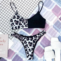 Bikini bralette noir à haut et bas imprimés léopard gris, posé à plat avec un livre et des sandales blanches