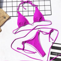Bikini string croisé sans armatures taille basse violet posé à plat, lacets longs déployés et slip à anneau