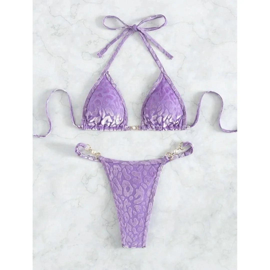 Bikini string triangle sans armatures imprimé léopard violet posé à plat sur marbre blanc, bretelles fines et anneaux dorés