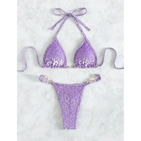 Bikini string violet imprimé léopard posé à plat sur du marbre blanc, lien latéral et bas à anneaux dorés