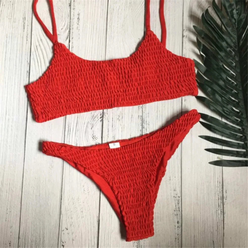 Bikini deux pièces texturé effet froissé rouge à plat sur un parquet clair, avec une feuille de palmier à côté