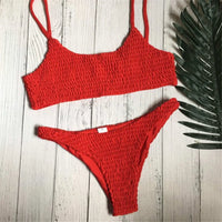 Bikini deux pièces texturé effet froissé rouge à plat sur un parquet clair, avec une feuille de palmier à côté