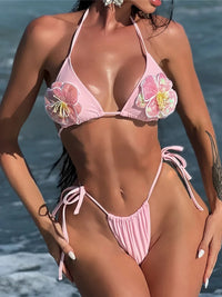Bikini triangle rose à grosses fleurs en relief et paillettes sur les bonnets, porté de face en bord de mer, bas à nouer