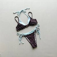 Bikini sans armatures à pois marron posé à plat sur fond gris, bordures bleu ciel et liens longs à nouer sur les côtés