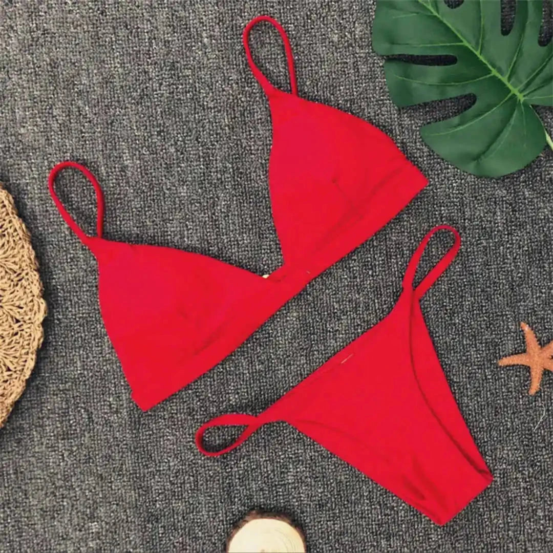 Bikini brésilien rembourré à taille basse rouge posé à plat sur tapis gris, fines bretelles et étoile de mer