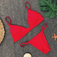 Bikini brésilien rembourré à taille basse rouge posé à plat sur tapis gris, fines bretelles et étoile de mer