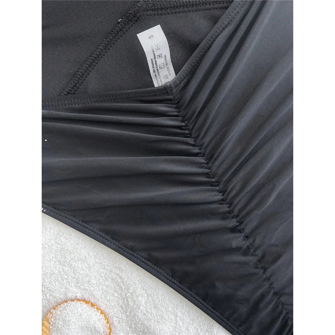 Gros plan sur le bas froncé du maillot une pièce noir, étiquette blanche visible sur l'intérieur du décolleté