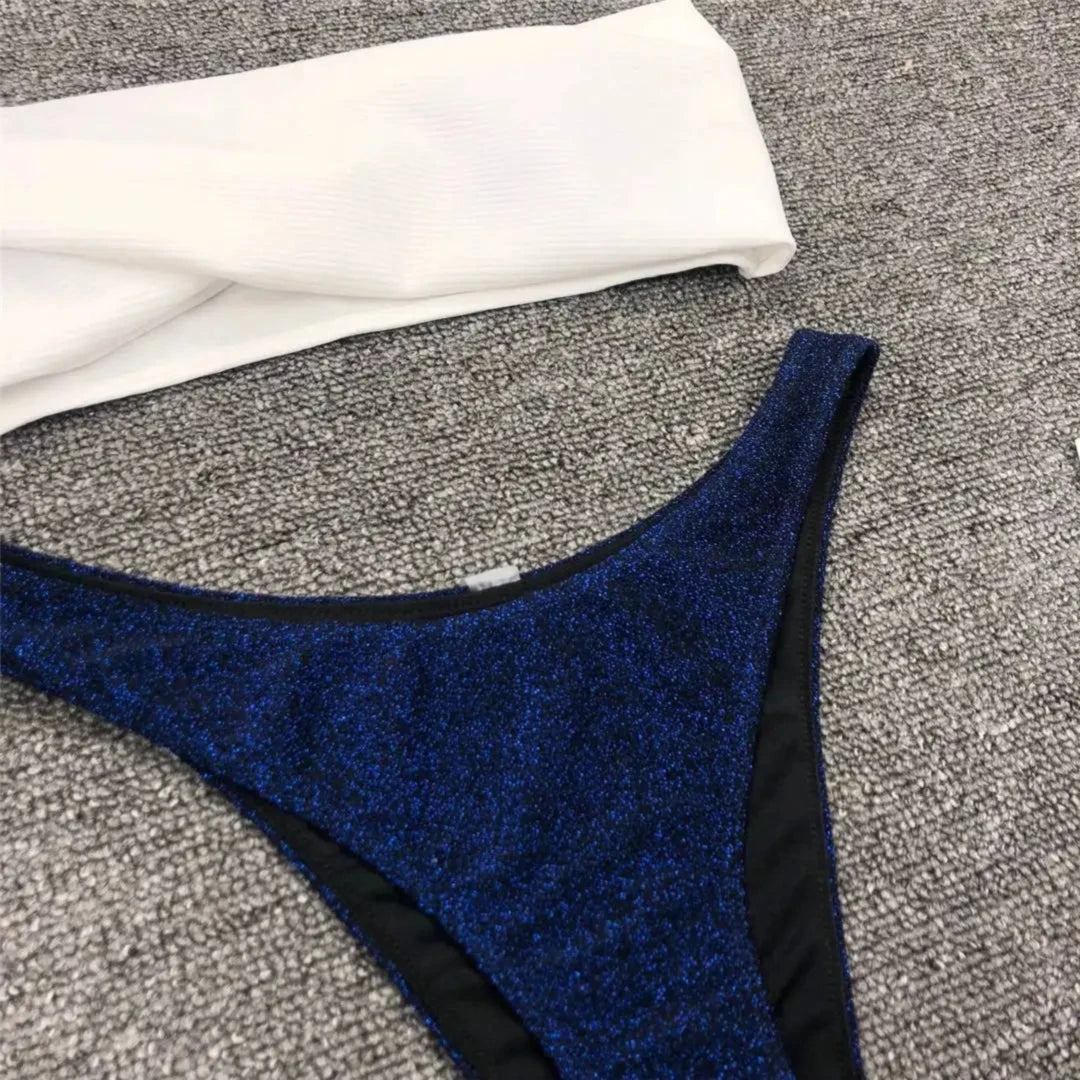 Gros plan sur le bas bleu marine pailleté et le haut blanc d'un bikini bandeau scintillant posé à plat