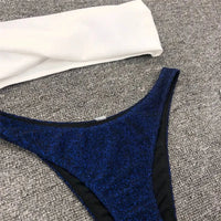 Gros plan sur le bas bleu marine pailleté et le haut blanc d'un bikini bandeau scintillant posé à plat