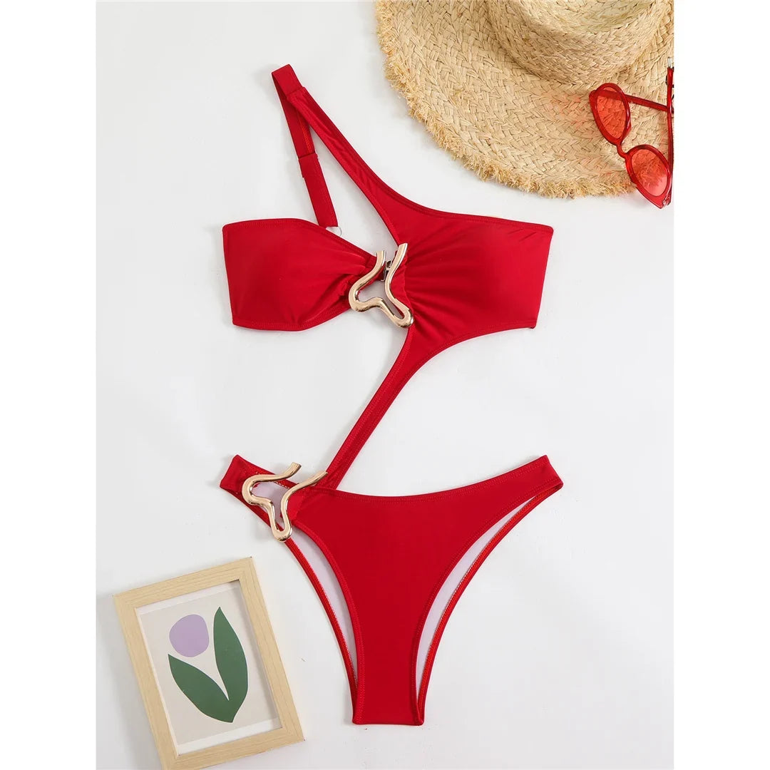 Maillot de bain une pièce asymétrique rouge posé à plat avec chapeau de paille, anneau doré au ventre et cadre illustré