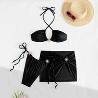 Maillot de bain trois pièces jupe halter à brides noir étalé à plat, haut à bretelles croisées et jupe portefeuille à ornements dorés