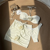 Maillot de bain trois pièces jupe fleurs en relief blanc cassé à plat sur un panier, avec coquillages et étoiles de mer