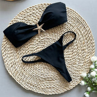 Bikini bandeau string échancré à étoile métallique noir posé à plat sur un tapis en osier, étoile dorée sur le haut