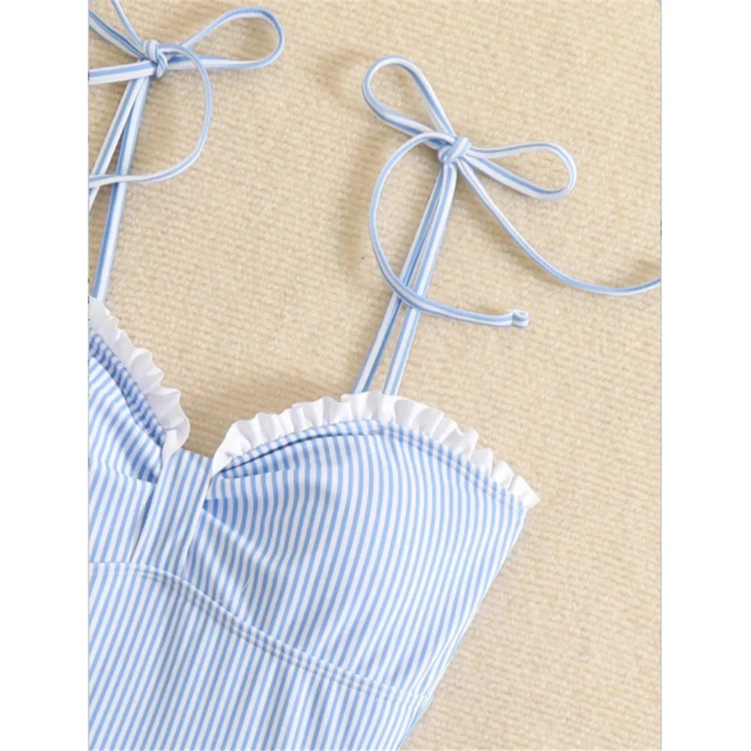 Gros plan sur le décolleté à volants blancs du maillot une pièce rayé bleu et les fines bretelles nouées en nœud