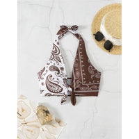 Haut de bikini tour de cou noué imprimé paisley marron et blanc posé à plat, pointes nouées sur du marbre blanc avec un chapeau