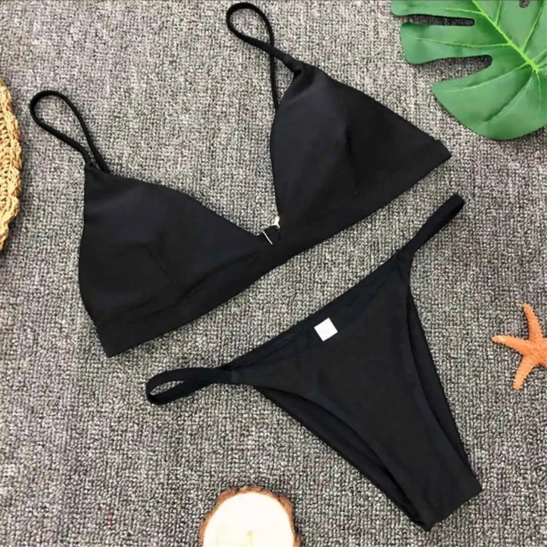 Bikini brésilien rembourré à taille basse noir posé à plat sur tapis gris, étoile de mer orange et rondin de bois