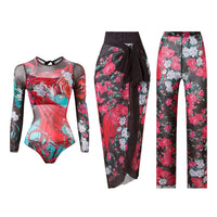 Maillot trois pièces manches longues imprimé fleurs roses sur fond noir, body, paréo et pantalon en mesh posés à plat