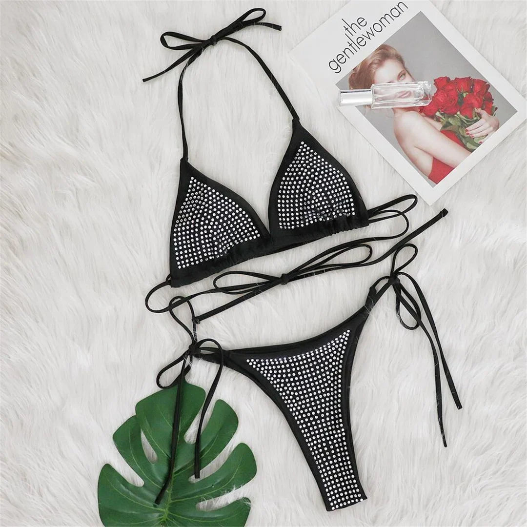 Bikini tour de cou noir à strass posé à plat sur une fourrure blanche, à côté d'une feuille verte