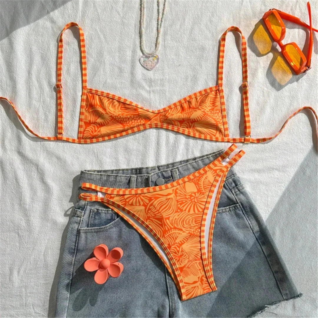 Bikini brésilien triangle orange imprimé posé à plat sur un short en jean, avec une fleur rose et des lunettes